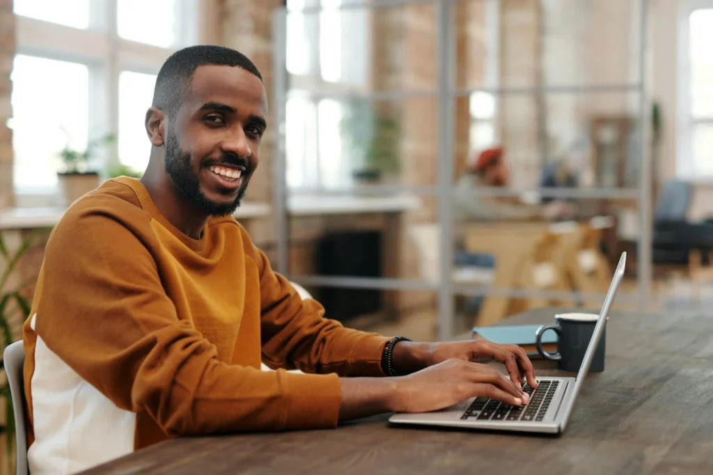 A web designer, smiling for the camera busy with his laptop